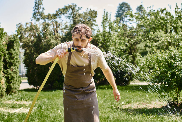 jardineiro barbudo em avental de linho água potável da mangueira depois de trabalhar no jardim, foto franca - Foto, Imagem