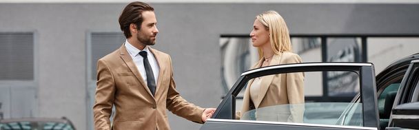 bearded stylish man and elegant blonde businesswoman holding hands near luxury car on street, banner - Photo, Image