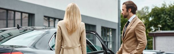 vousatý elegantní muž v obleku otvírající zadní dveře luxusního vozu v blízkosti blond obchodnice, prapor - Fotografie, Obrázek