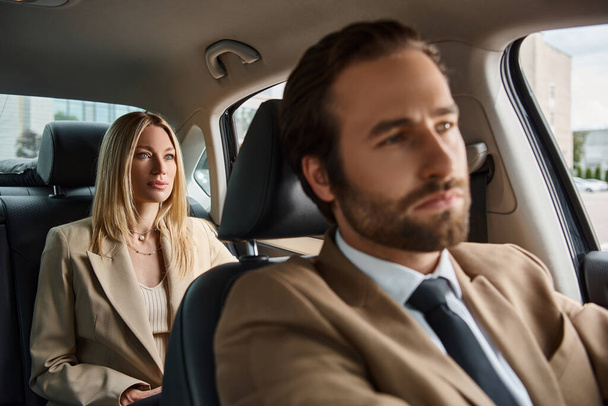 wazig elegante man in formele kleding rijden luxe auto met stijlvolle blonde zakenvrouw op de achterbank - Foto, afbeelding
