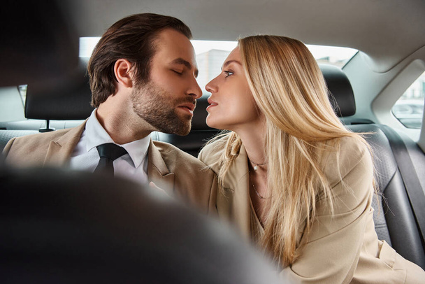 hombre de negocios elegante y atractiva mujer rubia sentada cara a cara en un coche de lujo, seducción - Foto, imagen