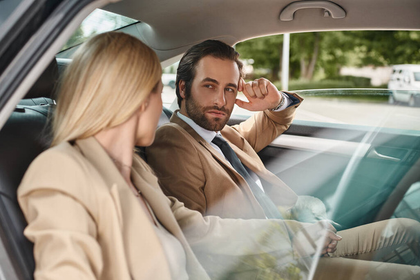 όμορφος επιχειρηματίας κοιτάζοντας ξανθιά γυναίκα συνάδελφο, ενώ αποπλάνηση της στο αυτοκίνητο, έλξη - Φωτογραφία, εικόνα