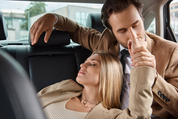 uomo d'affari in giacca e cravatta baciare mano di donna bionda appassionata durante il viaggio in auto, seduzione - Foto, immagini