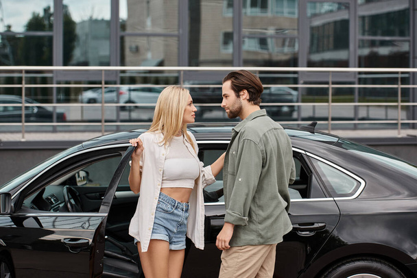 mulher loira e homem barbudo em roupas casuais elegantes olhando um para o outro perto do carro, atração - Foto, Imagem