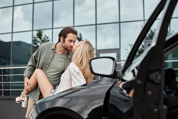 homme barbu tendance et beau en vêtements décontractés séduire femme blonde près de la voiture dans la rue urbaine - Photo, image
