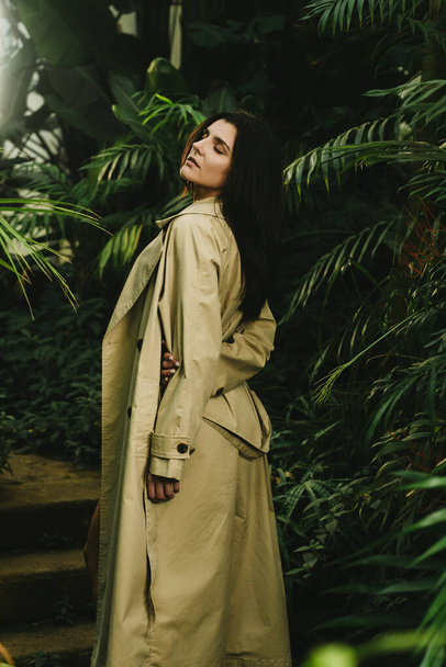 Mulher sexy em um casaco bege posando em um jardim tropical. Conceito de tiro moda - Foto, Imagem