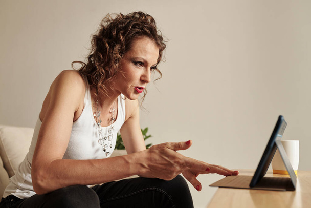 Емоційна стильна зріла жінка дивиться шокуючі новини на цифровому планшеті - Фото, зображення