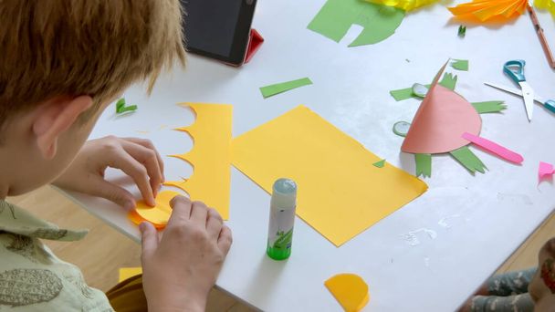 Dzieciak tworzy aplikację z kolorowym papierem i klejem. Pojęcie hobby i edukacji. Wysokiej jakości zdjęcie - Zdjęcie, obraz