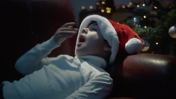 Karácsonyi kalapos gyerek elalszik a fa alatt..  - Felvétel, videó