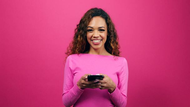 Linda mujer joven vestida de rosa en citas aplicación de teléfono celular, estudio. Foto de alta calidad - Foto, Imagen
