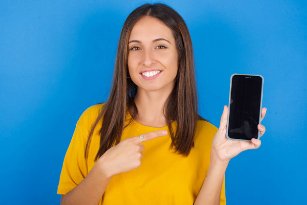 Lächelnde junge Frau, die auf den leeren Telefonbildschirm zeigt. Werbe- und Kommunikationskonzept. - Foto, Bild