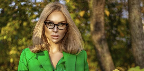 Piękna kobieta w zielonym płaszczu i eleganckiej odzieży jest pozowanie na zewnątrz w słoneczny jesienny dzień. - Zdjęcie, obraz