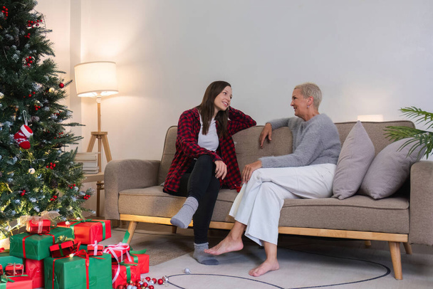 Mujer joven y madre sentado y hablando en la sala de estar con árbol de Navidad y cajas de regalo. mujer joven hablando Relájese en el sofá con mamá en el día de Navidad o cualquier día festivo.. - Foto, imagen