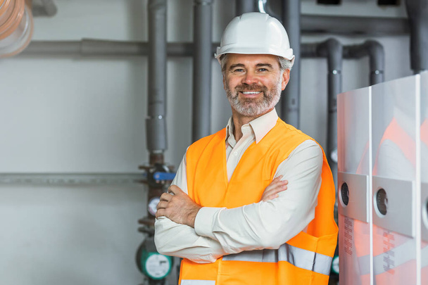 portrait of mature senior gray haired refinery worker standing inside power plant with crossed hands - Photo, Image