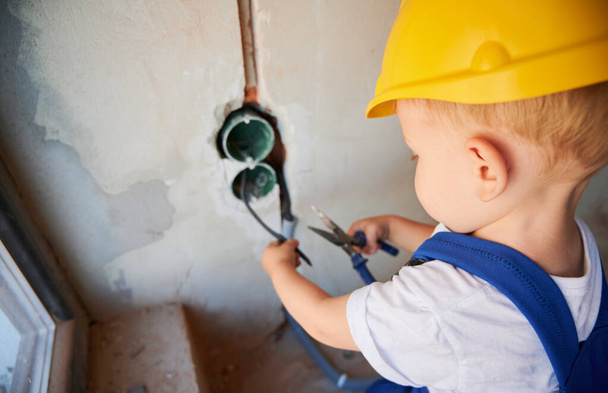 Zbliżenie elektryka ciąć druty szczypce w budynku w trakcie budowy. Dzieciak w kasku mocującym kable w ścianie podczas remontu domu. - Zdjęcie, obraz
