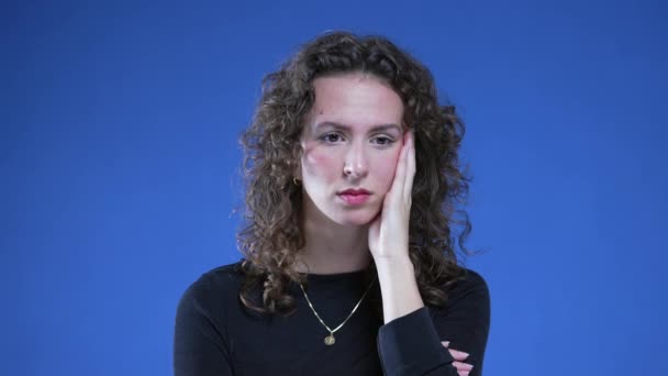 Preoccupied woman feeling anxiety while standing on blue background. Close-up face of person experiencing mental tension and preoccupation - Footage, Video
