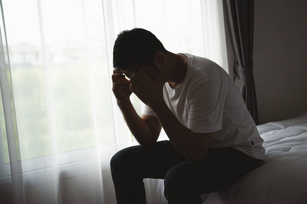 Silhouette depressiven Mann traurig auf dem Bett im Schlafzimmer sitzen. Traurige asiatische Männer, die unter Depressionen leiden, wachen auf und sitzen allein auf dem Bett im Schlafzimmer. Depressionen Gesundheit Menschen Konzept. - Foto, Bild