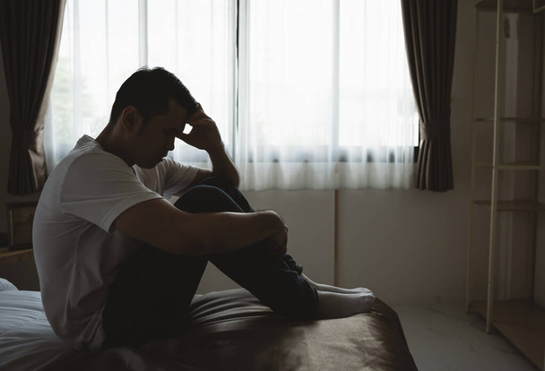 Silhouette depressziós férfi szomorúan ül az ágyon a hálószobában. Szomorú ázsiai férfiak depresszióban szenvednek álmatlanságban és egyedül ülnek az ágyon a hálószobában. Depresszió egészségügyi emberek koncepciója. - Fotó, kép