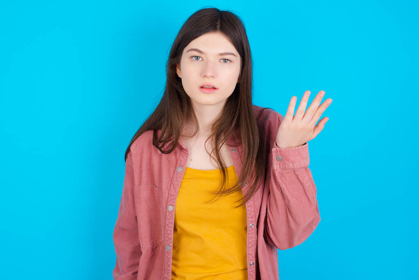 Studio shot of frustrated young caucasian girl wearing pink shirt isolated over blue background gesturing with raised palm, frowning, being displeased and confused with dumb question. - 写真・画像