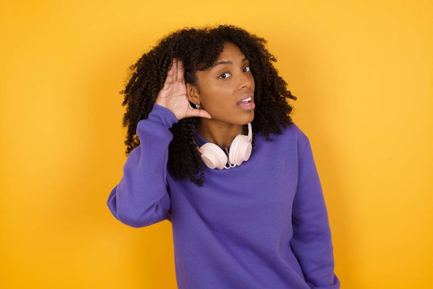 portret młodej, ekspresyjnej, afrykańskiej kobiety ze słuchawkami na żółtym tle - Zdjęcie, obraz