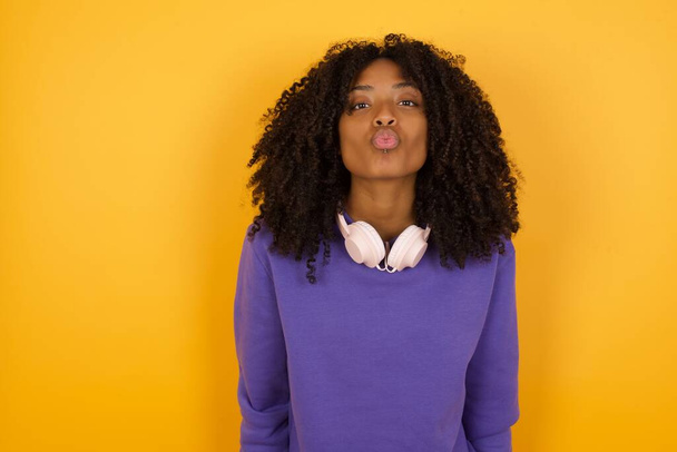 портрет молодої виразної афроамериканки з навушниками на жовтому фоні - Фото, зображення