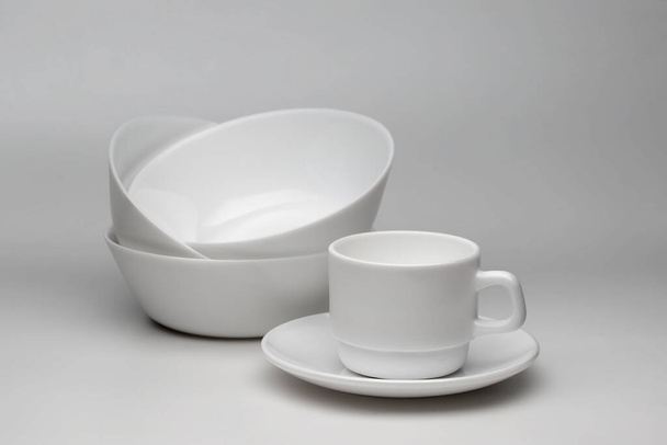 Mély fehér tányérok és fehér kávéscsésze és csészealj könnyű háttérrel - Fotó, kép