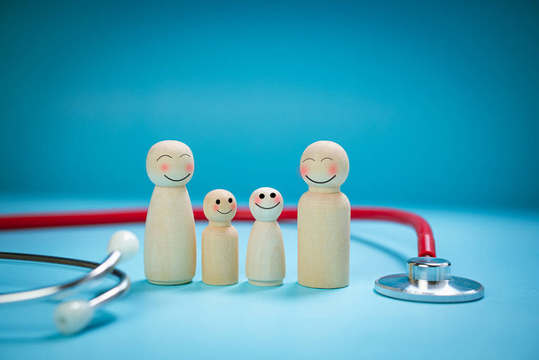 Pojetí zdravotního pojištění, dřevěné panenky, rodina rodičů a dětí, šťastně se usmívající tváře, obklopené stetoskopy, jasně modré pozadí. Koncept ochrany rodiny. Postarejte se o bezpečnost. - Fotografie, Obrázek