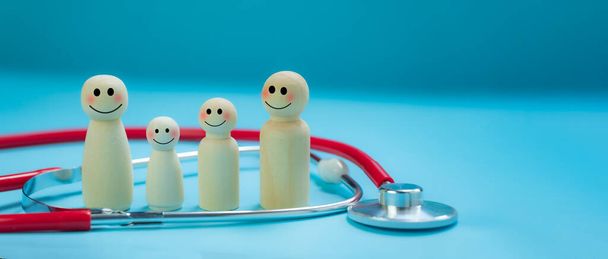 Health insurance concept, wooden dolls, family of parents and children, happy smiling faces, surrounded by stethoscopes, bright blue background. Family protection concept. Take care of safety. - Photo, Image