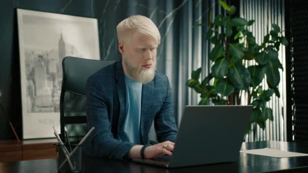Sebevědomý albínský obchodník píšící na notebooku v kanceláři. Vážný muž podnikatel odpovídá na zákaznické e-maily. Stylový manažer se soustředil na práci. Zaostřený muž v obleku pomocí PC u stolu  - Záběry, video