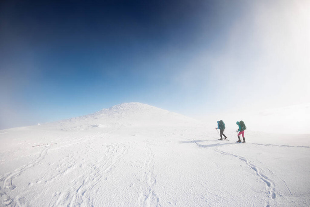 登山者は雪の中で山を登る。 ウィンターマウンテン。 雪の中を歩いている2人の女の子. 登山設備について。 冬の山でハイキング. - 写真・画像