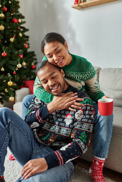 κάθετη λήψη ευτυχισμένου Αφροαμερικανού ζευγαριού με ζεστά πουλόβερ που αγκαλιάζει με κλειστά μάτια, Χριστούγεννα - Φωτογραφία, εικόνα