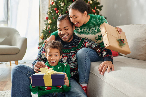 familia afroamericana alegre asombrada abrazándose y mirando sorprendida en regalo de Navidad - Foto, Imagen