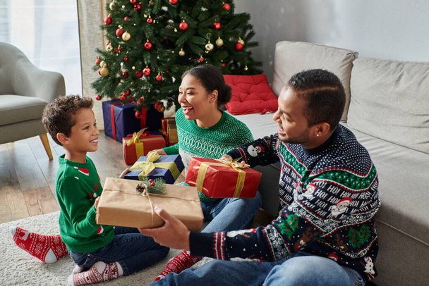 όμορφη χαρούμενη αφροαμερικανική οικογένεια ανταλλαγή δώρων δίπλα στο χριστουγεννιάτικο δέντρο με μπιχλιμπίδια - Φωτογραφία, εικόνα