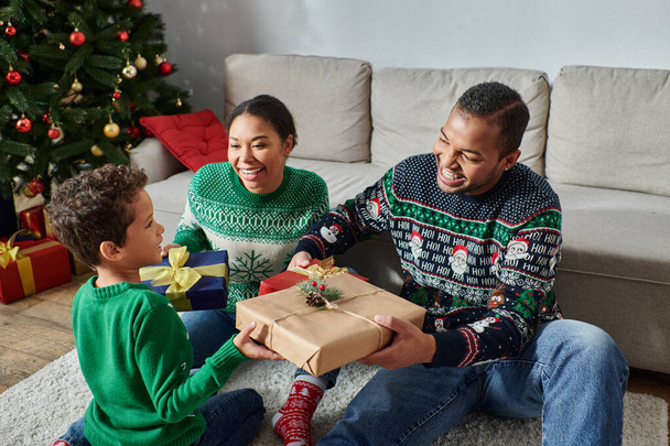 веселі афроамериканські батьки обмінюються подарунками зі своїм сином біля святкової ялинки, Різдво - Фото, зображення
