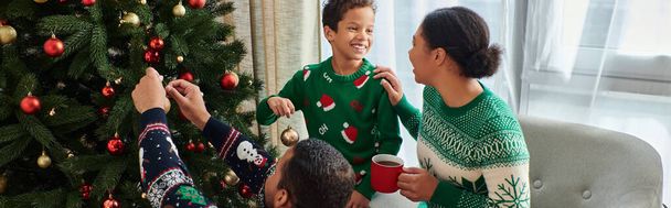 allegra donna afroamericana guardando il figlio e il marito che decorano l'albero di Natale, striscione - Foto, immagini