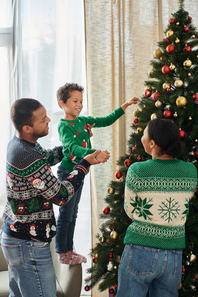 tiro vertical da família afro-americana sorrindo alegremente um para o outro decorando árvore de Natal - Foto, Imagem