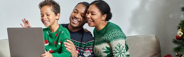 Χαρούμενοι Αφροαμερικανοί γονείς που κρατάνε το γιο τους σε γύρους βλέποντας Χριστουγεννιάτικη ταινία στο laptop, banner - Φωτογραφία, εικόνα