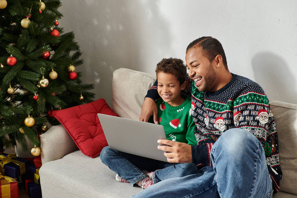 happy cute african american boy watching Christmas comedy movie on laptop with his cheerful father - Foto, Imagem