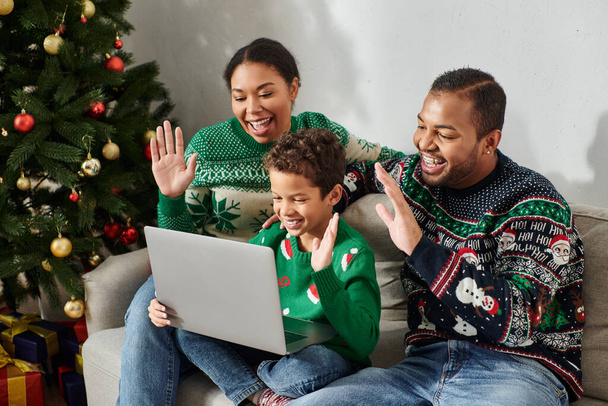 iloinen moderni afrikkalainen amerikkalainen perhe viihtyisissä villapaidoissa heiluttaen hei kannettavan tietokoneen kameralla, joulu - Valokuva, kuva