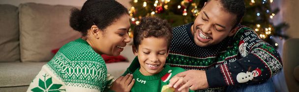 vrolijk Afrikaans amerikaanse familie in gezellige truien glimlachen en knuffelen liefdevol, Kerstmis, banner - Foto, afbeelding