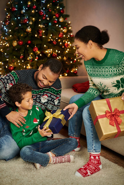 colpo verticale di madre afroamericana che fa un regalo al figlio mentre il padre lo abbraccia, Natale - Foto, immagini