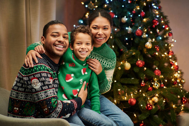 modern Afrikaans amerikaans gezin in warme truien glimlachen op de camera terwijl knuffelen warm, Kerstmis - Foto, afbeelding