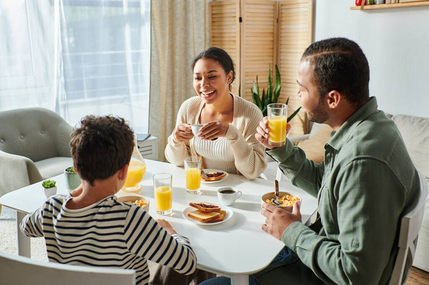 陽気な現代アフリカ系アメリカ人の家族が一緒に朝食を食べ,笑顔で - 写真・画像