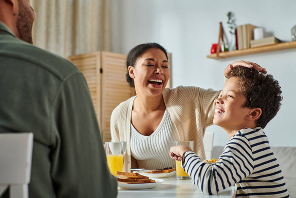 vista recortada del hombre afroamericano sentado en la mesa de desayuno frente a su alegre esposa e hijo - Foto, imagen