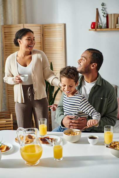 вертикальный снимок красивой веселой африканской семьи смеющейся и хорошо проводящей время за завтраком - Фото, изображение