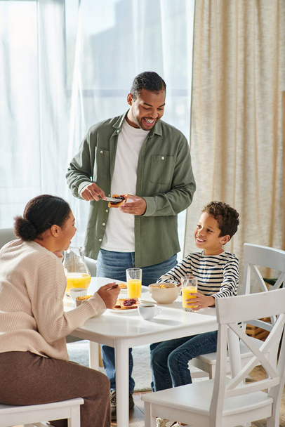 вертикальный снимок красивой африканской американской семьи, счастливо улыбающейся, завтракающей - Фото, изображение