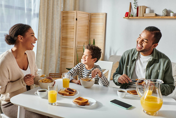 美しい現代アフリカ系アメリカ人の家族がおいしい朝食を食べながら話したり笑ったり - 写真・画像