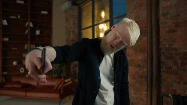 Porträt des hübschen Albino-Typen Social-Media-Blogger macht Selfie auf dem Smartphone in der Nacht Fenster. Lässiger männlicher Influencer, der lächelnd vor der Kamera posiert. Trendiger Mann mit Handy-Selfie-Fotos auf Dachboden - Filmmaterial, Video