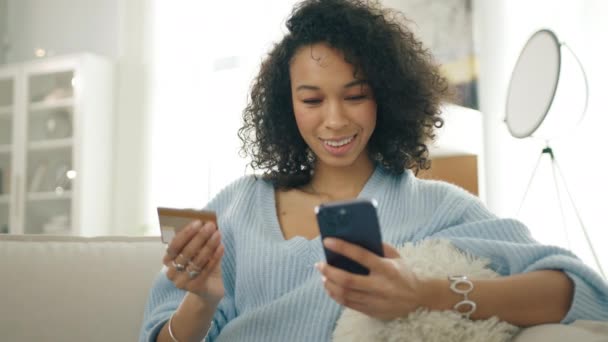 Smiling beautiful dark skinned girl making purchase on smartphone receiving cashback 4K. Happy elegant young multi racial woman holding credit card using instant mobile payments in modern apartment - Footage, Video