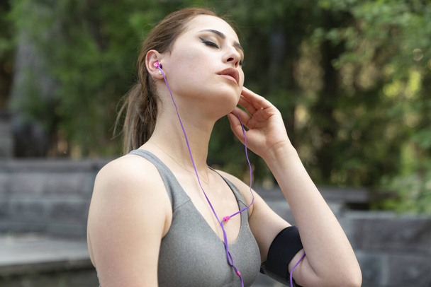 atleta femenina que usa ropa deportiva y usa un teléfono inteligente para escuchar música - Foto, imagen